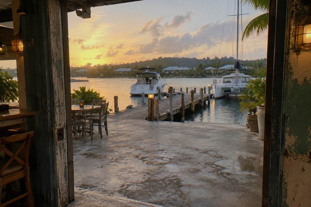 A wooden dock and restaurant terrace beside a lagoon with calm water and moored boats in evening light