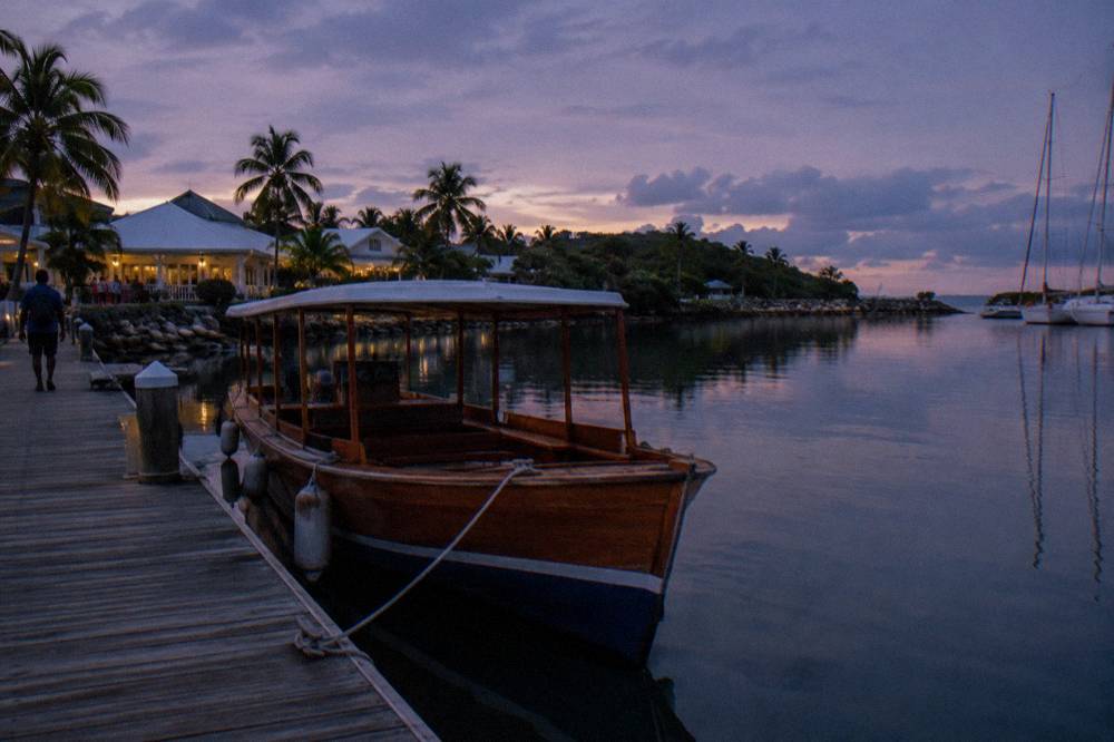 A wooden tour boat at a marina dock at dusk with still water and a dimming sky