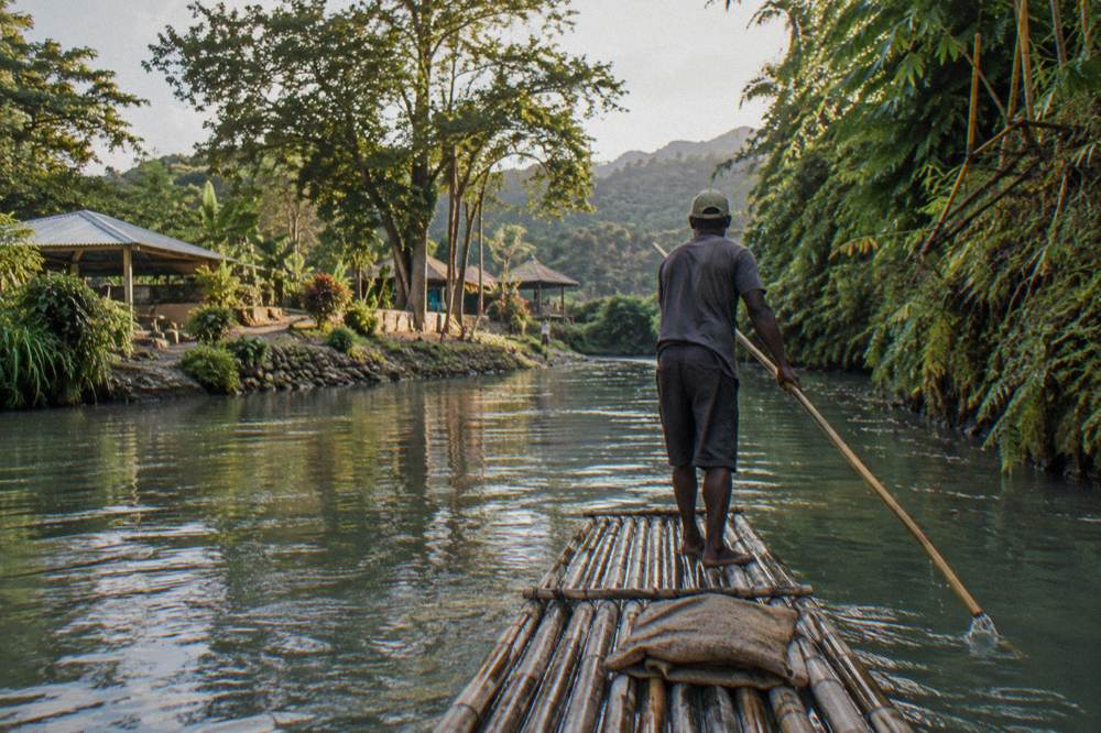 A bamboo raft drifting on a calm river between green banks in late afternoon light