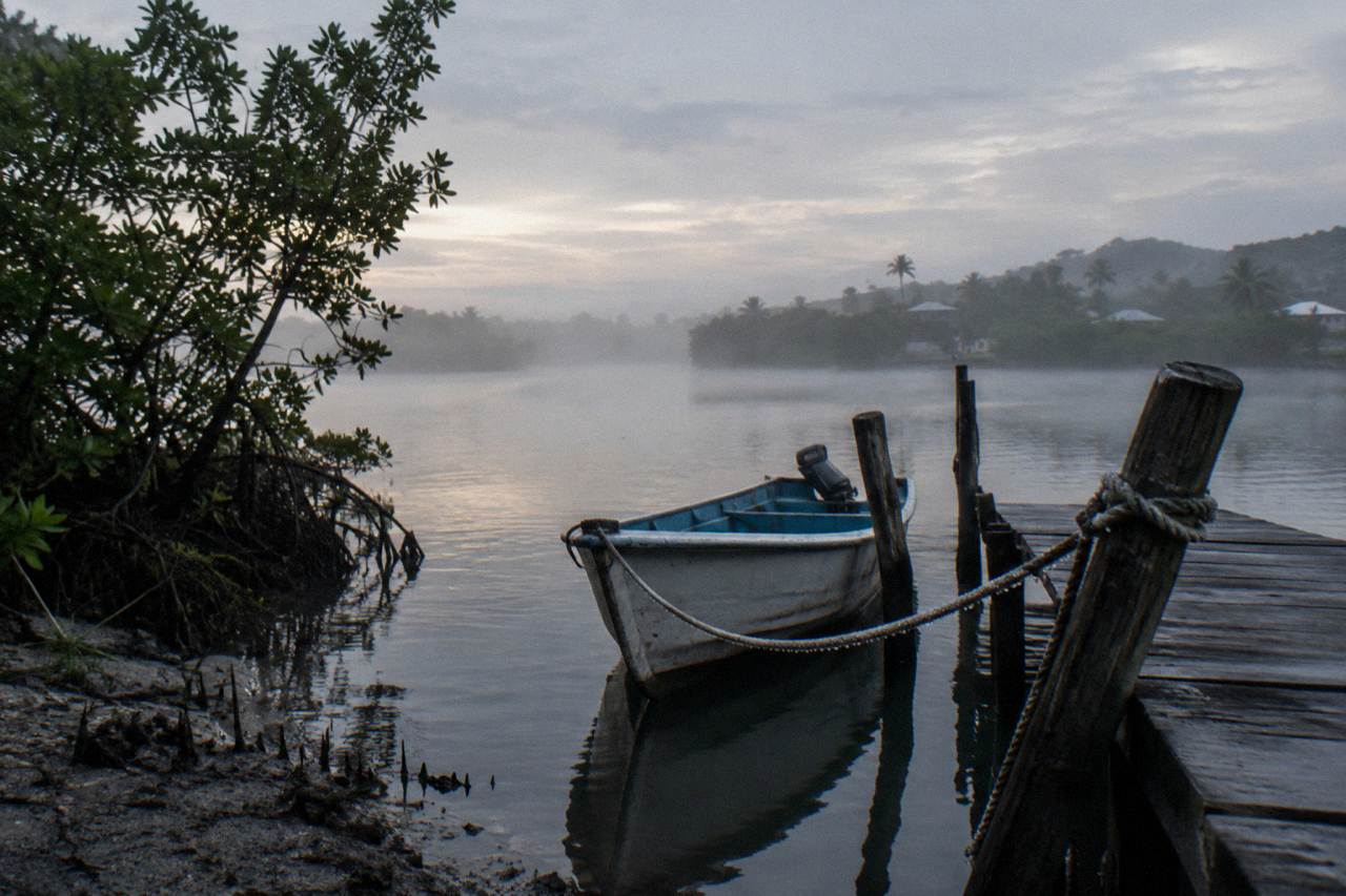 A calm tropical lagoon at dusk with mangroves along the shore and a small boat resting at a wooden dock