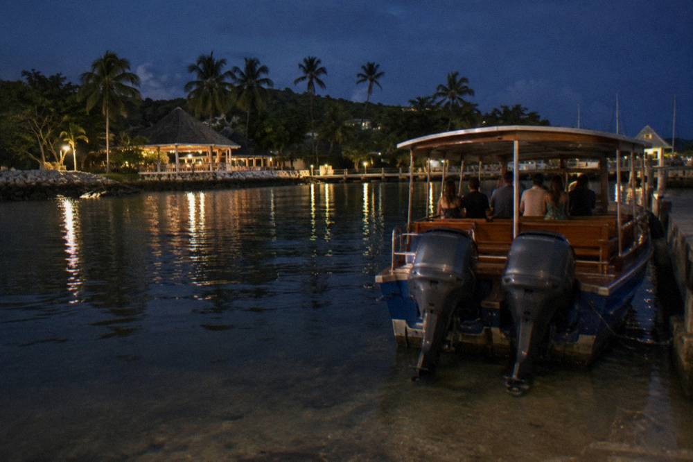 Wooden tour boat idling on still dark water with guests at the rail at night