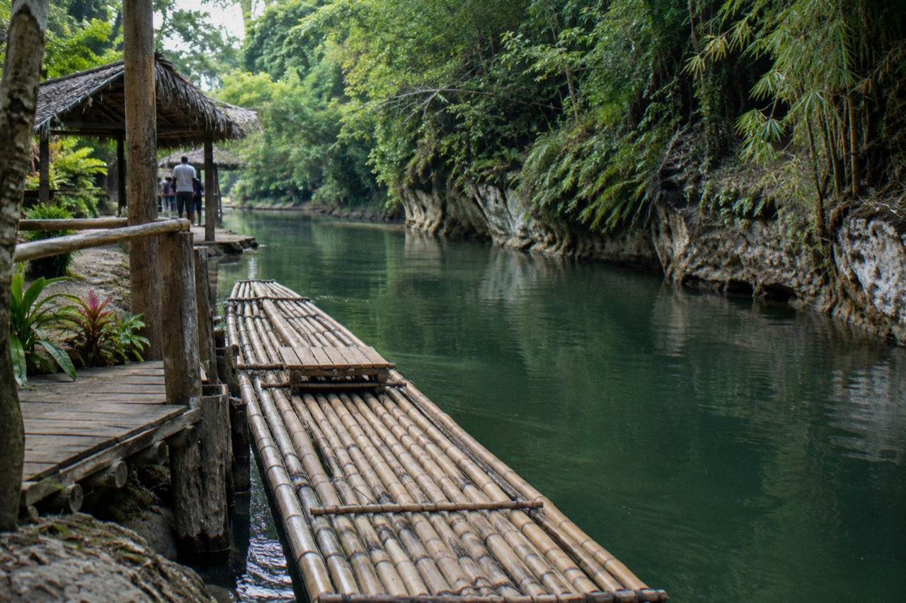 A bamboo raft resting on a calm green river with dense tropical forest on both banks