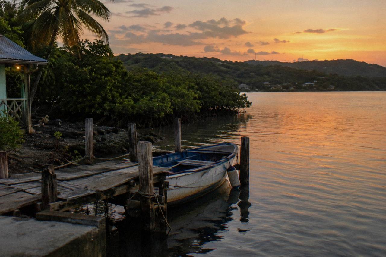 A calm lagoon at dusk with a small boat resting at a wooden dock and mangroves along the shore