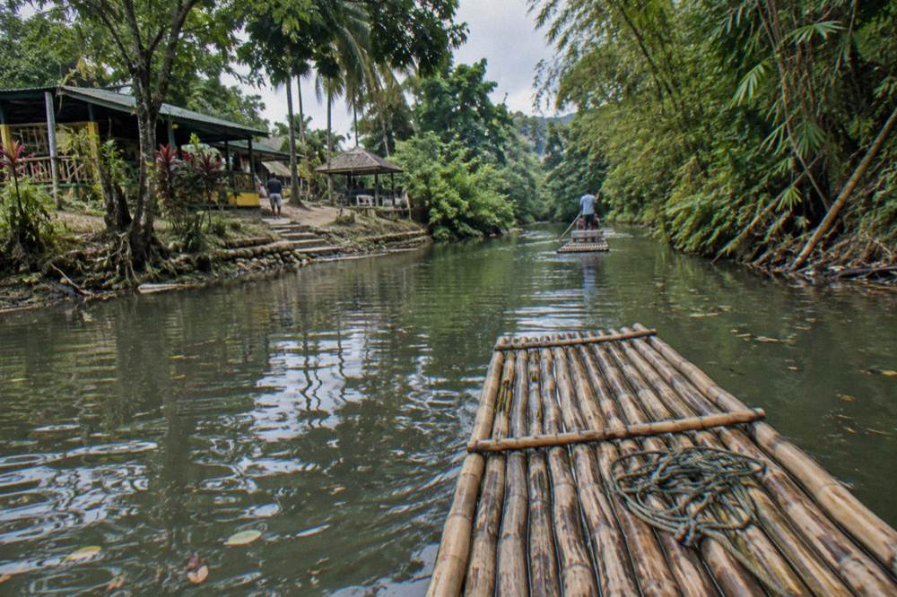 Wooden bamboo raft floating on a calm green river between trees