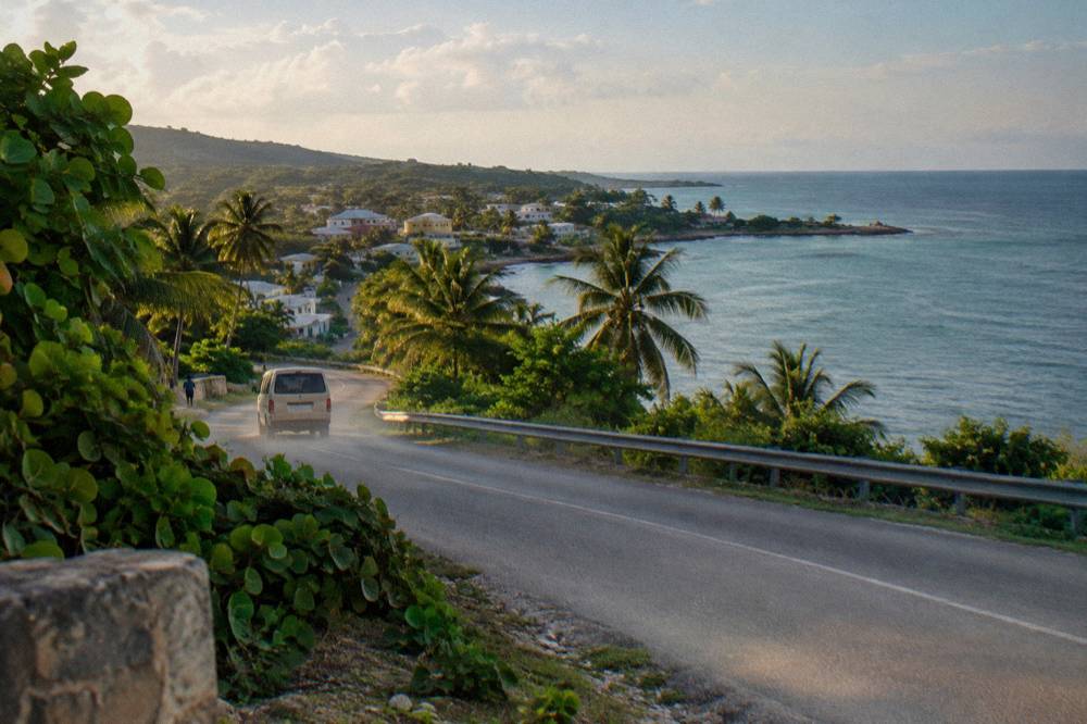 A coastal highway curving along a shoreline with palm trees and calm sea at late afternoon