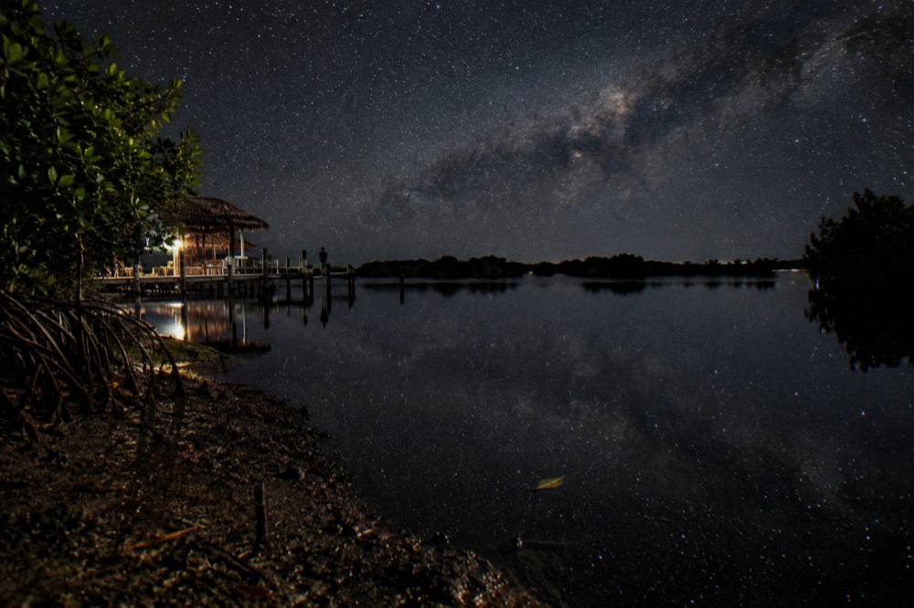 A dark night sky over calm water with a bright band of stars reflected on the surface