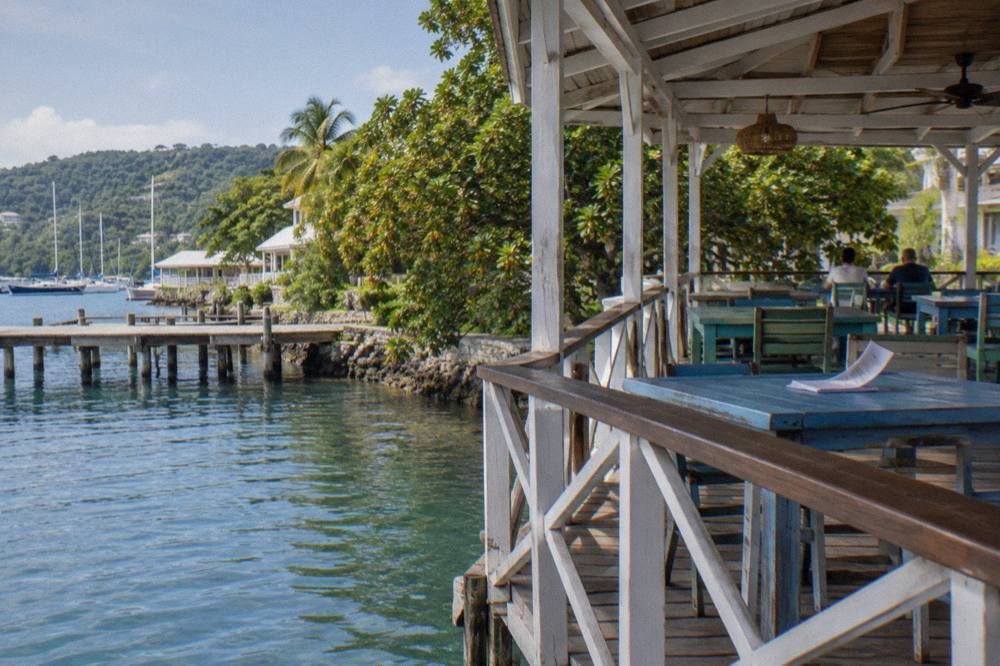 Open sided restaurant deck above still lagoon water with wooden tables and moored boats