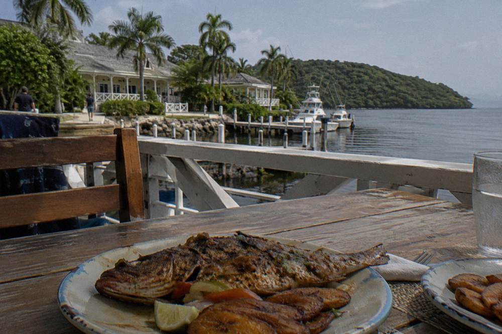 Grilled fish and side dishes plated on a wooden table overlooking dark water