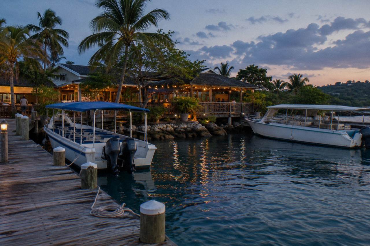 Wooden dock and moored tour boats on a calm lagoon at dusk with a restaurant deck glowing in the background