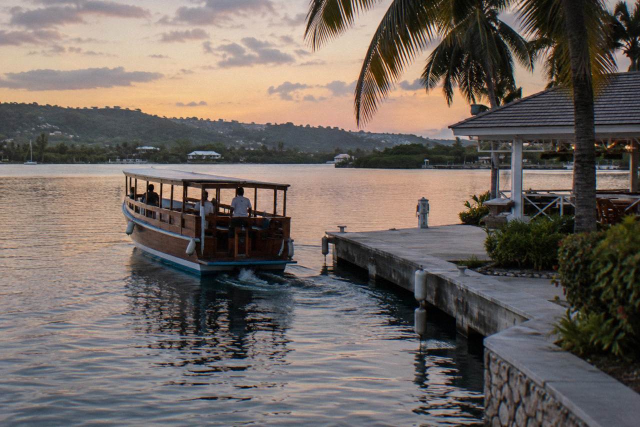 A wooden tour boat leaving a dark marina dock at dusk with still water ahead