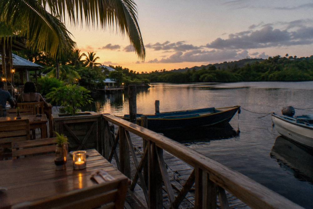 An evening restaurant terrace beside a dark tropical lagoon with boats at a dock