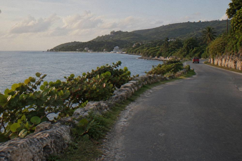 A coastal road curving past green hills toward a calm bay in late afternoon light