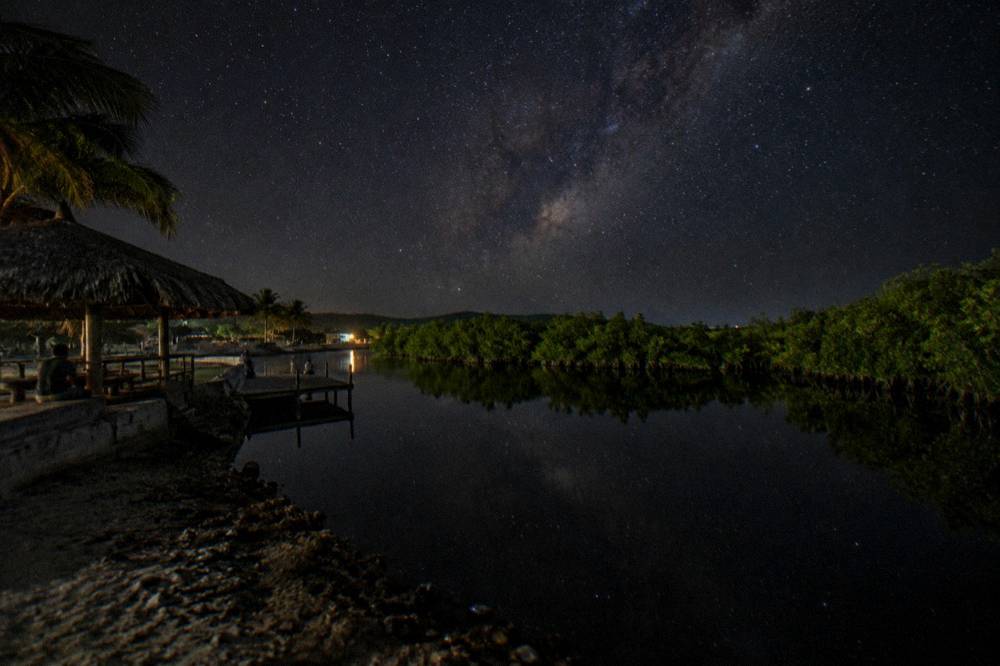 A dark night sky over still water with a faint band of the Milky Way above the lagoon