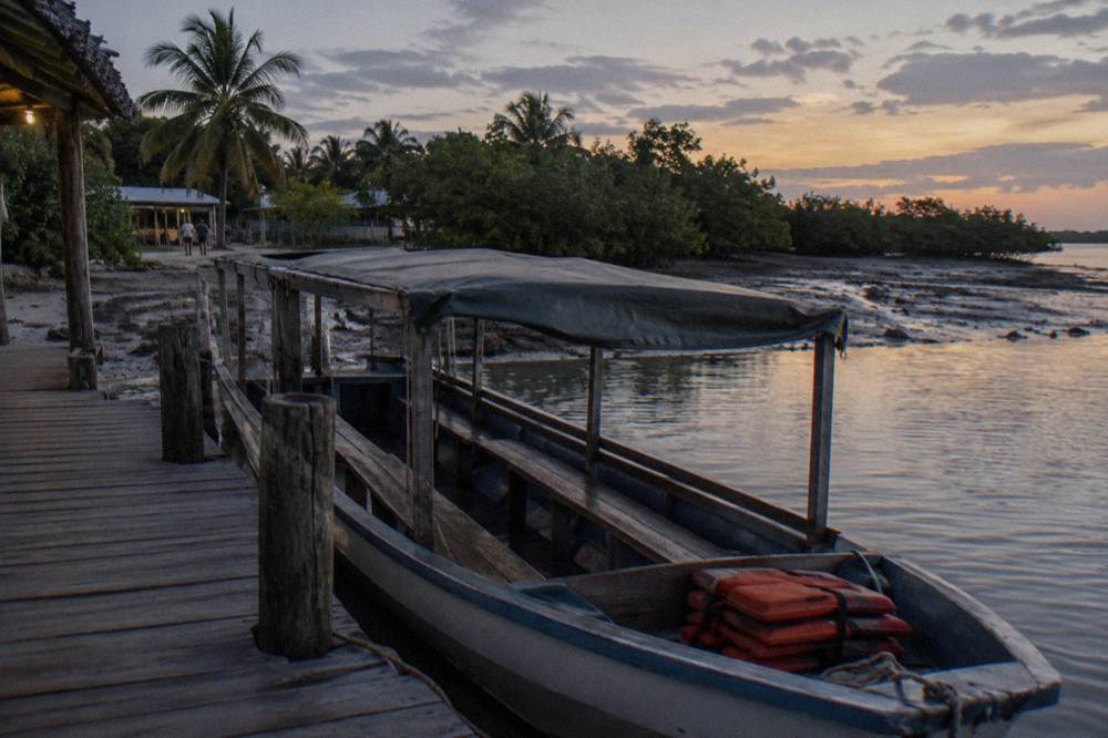 A covered wooden boat with bench seating moored at a dock before a night tour