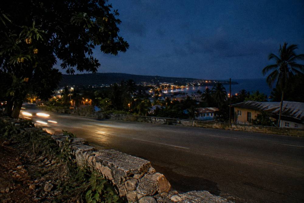 Nighttime coastal highway with headlights and distant town lights