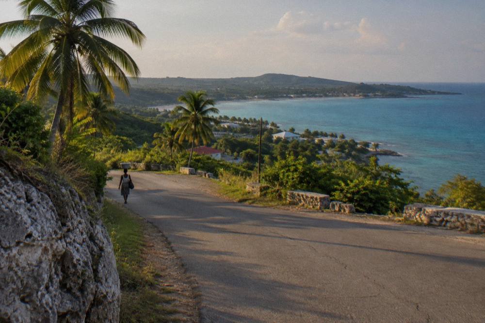 A coastal road curving past green hills toward a distant bay in late afternoon light