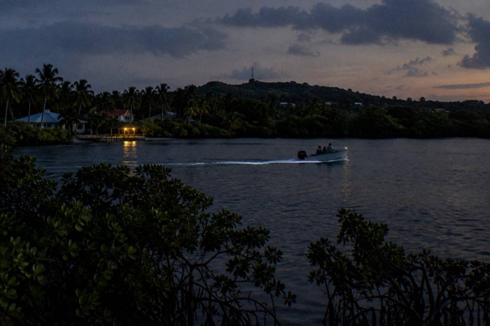 A small boat crossing glowing water with a trail of light behind the propeller