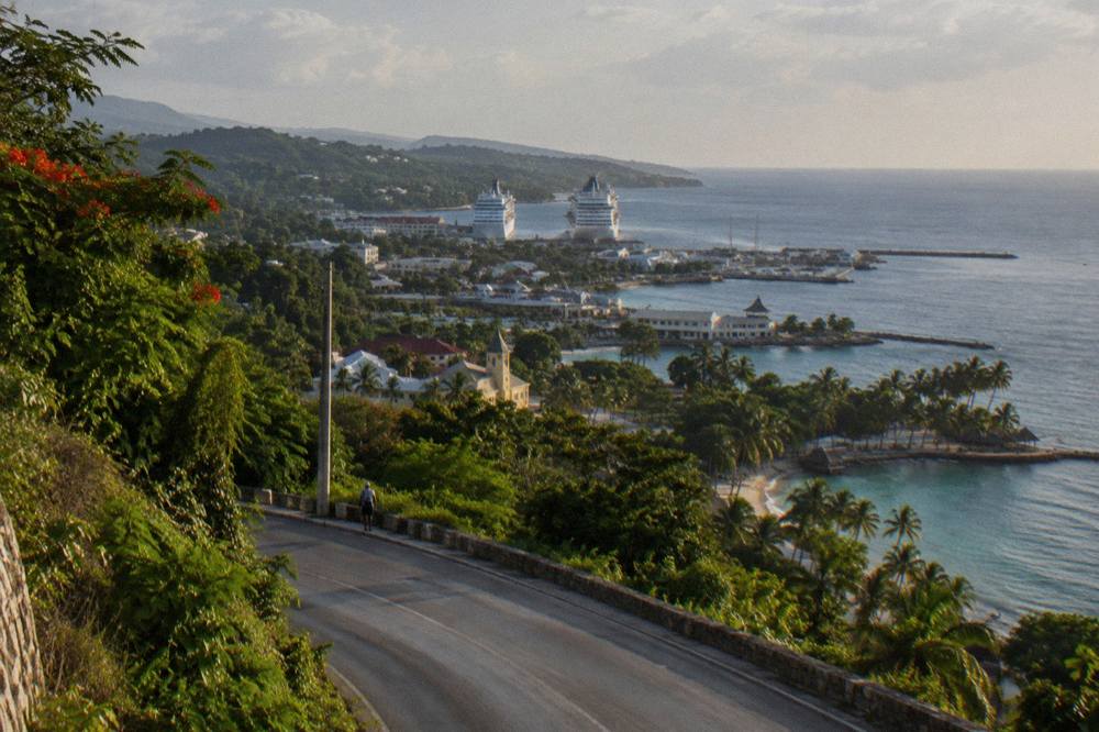 A coastal highway curving along a green hillside above the Caribbean sea in late afternoon light