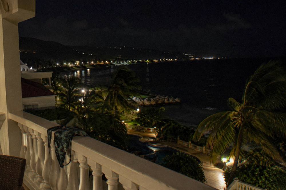 A resort balcony at night overlooking a dark sea with distant lights along the coast