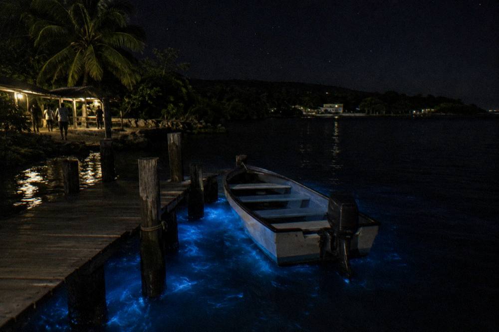 A small motorboat moored at a wooden jetty at night with blue glow around the pilings