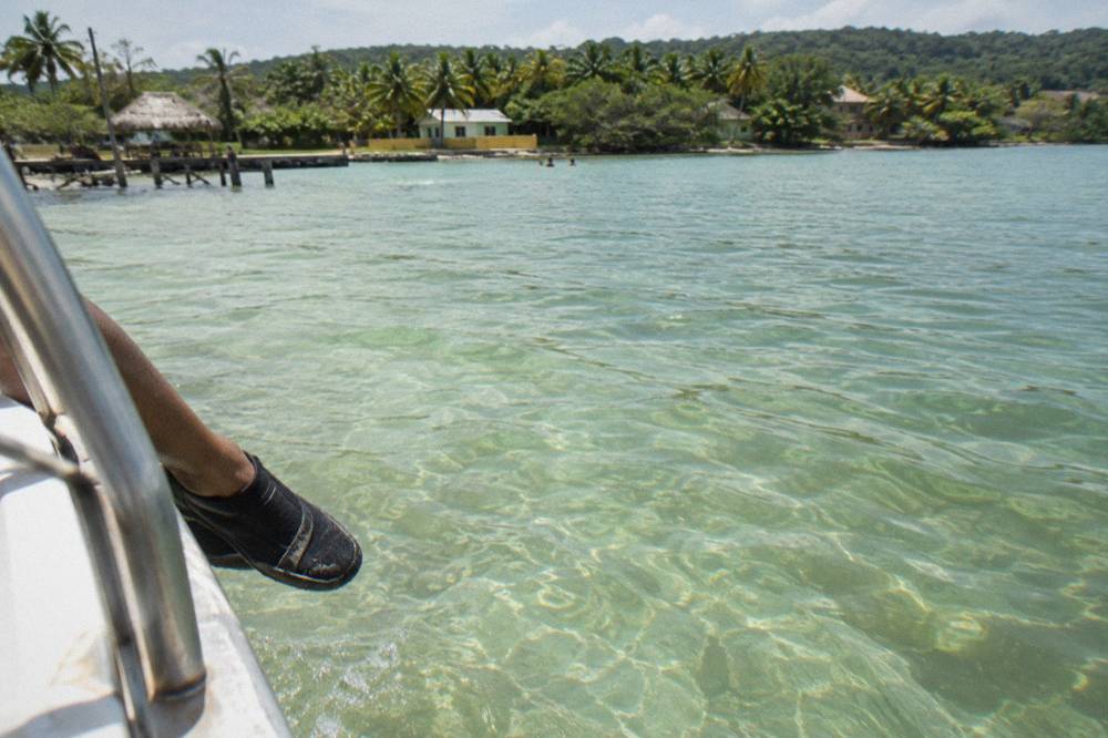 Shallow calm lagoon water over a soft sandy floor seen from a boat rail