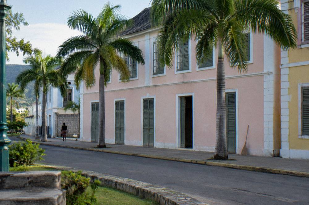 A quiet Jamaican coastal town street with pastel buildings and palm trees in early evening light