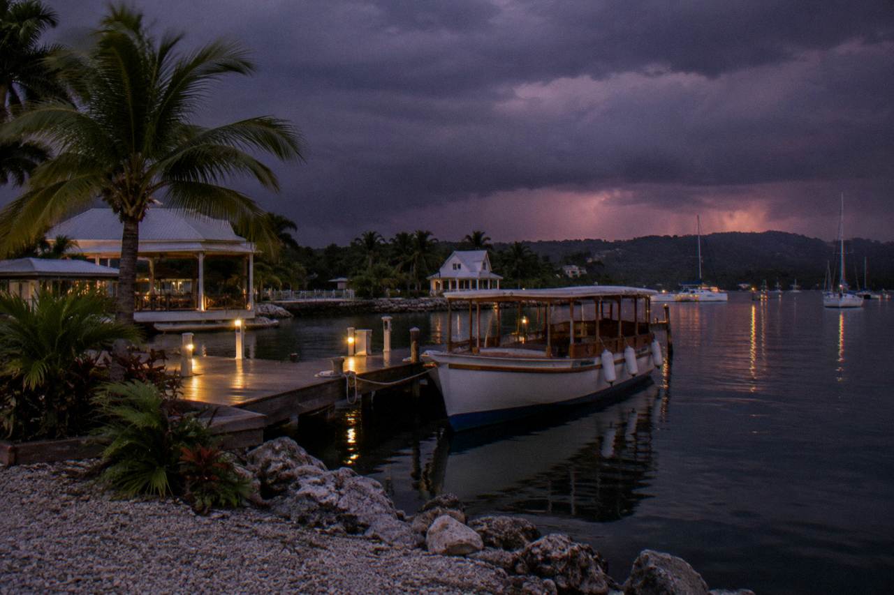 A wooden tour boat resting on calm dark lagoon water beside a lit marina dock at dusk