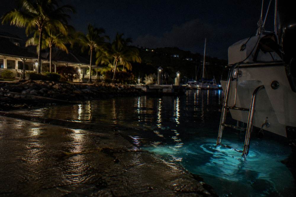 Still dark lagoon water at night reflecting a faint blue glow near a boat ladder