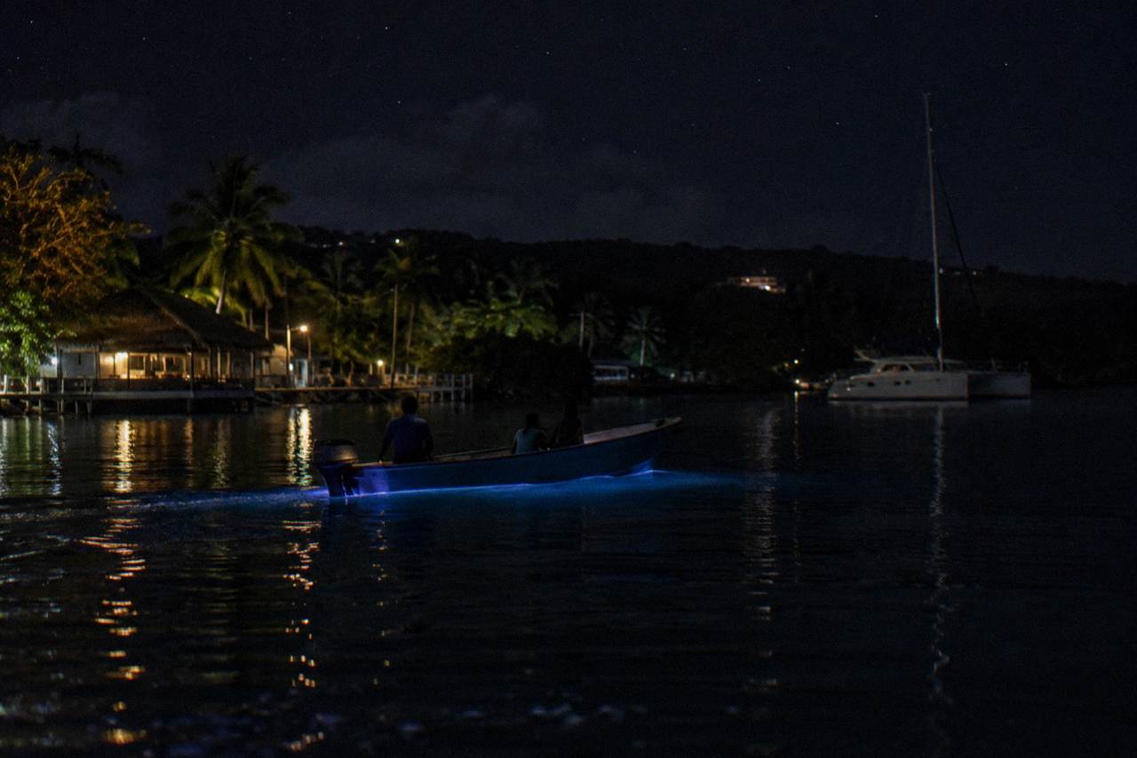 Boat on a dark lagoon at night with faint blue glow around the hull