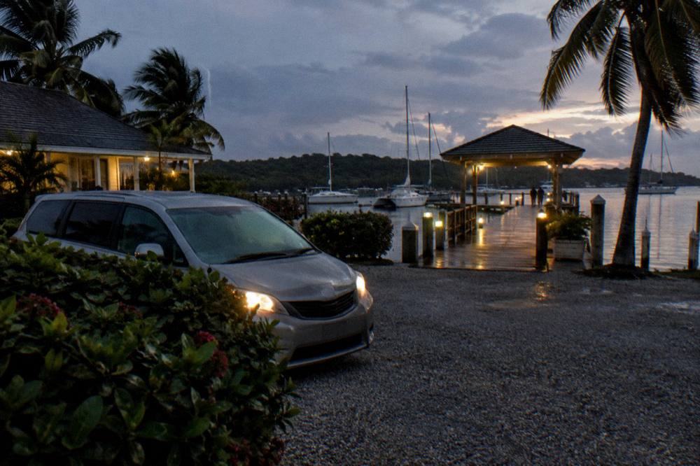 A private minivan parked on a dark roadside near a lit marina entrance