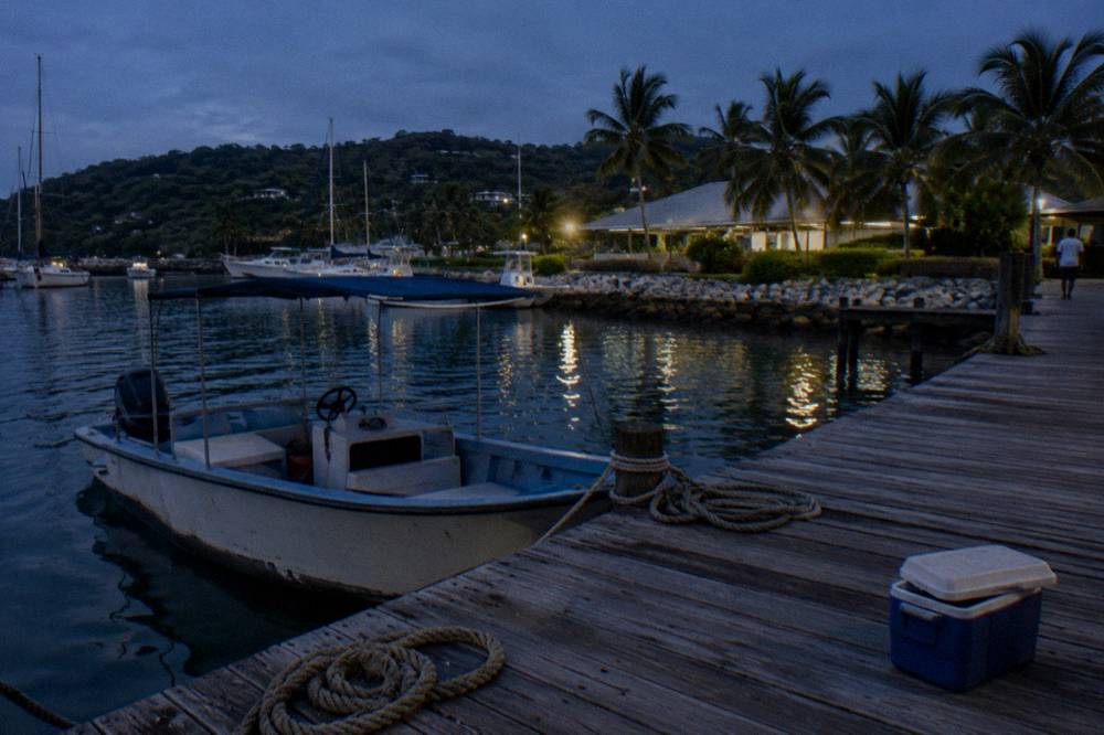 A small open tour boat at a wooden marina dock under a dark evening sky