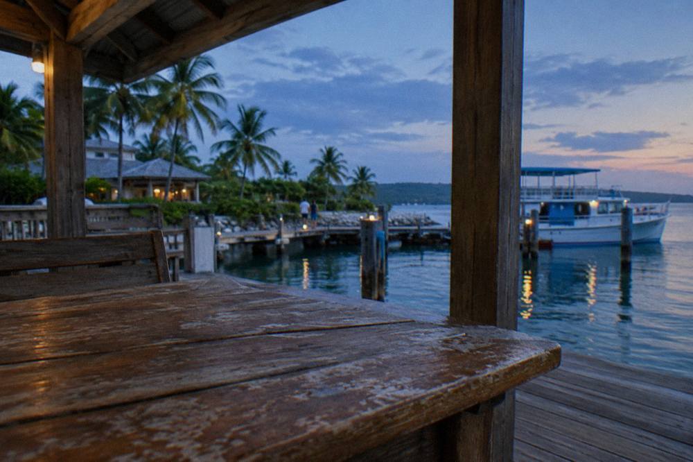 Folded dark towels and swimwear on a wooden bench beside a dock at dusk