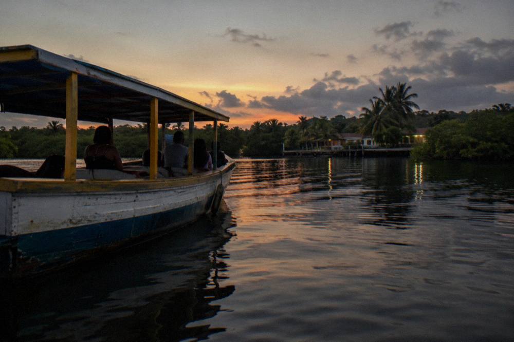 A wooden tour boat on dark calm lagoon water with the shoreline barely visible at dusk
