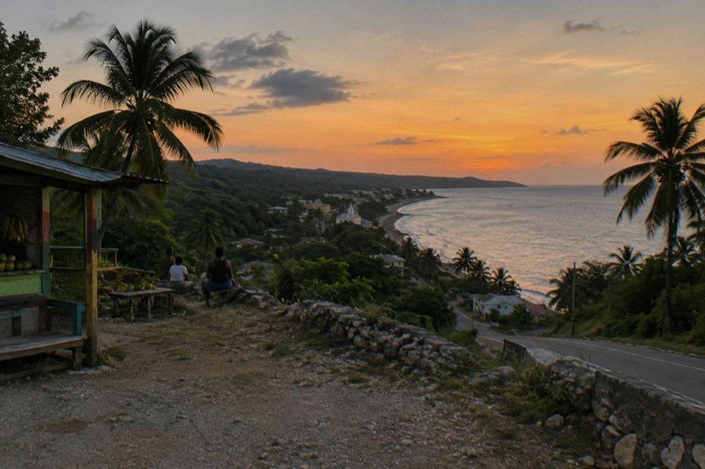 A coastal highway at dusk curving along the shoreline with palm trees